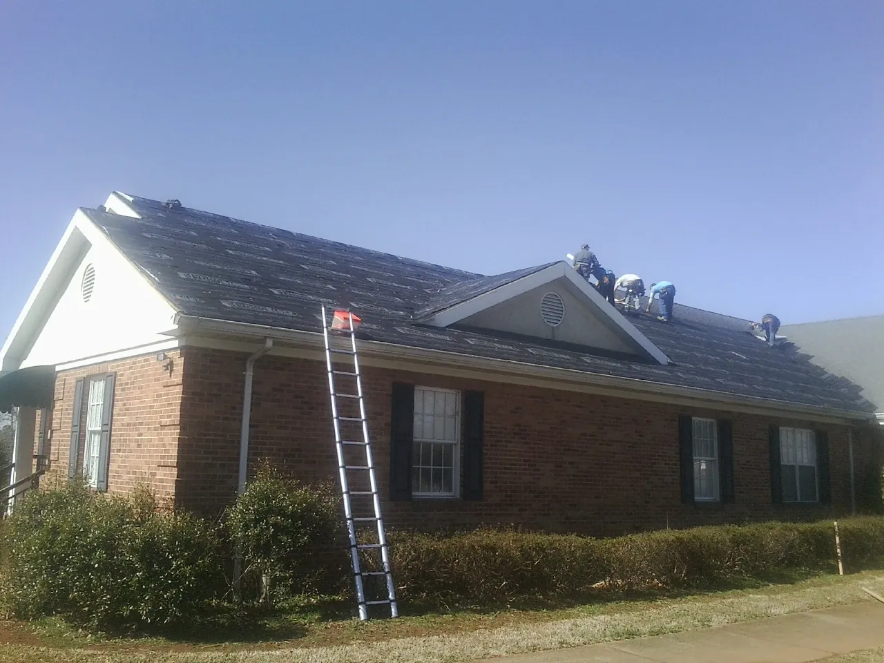 Crew tearing shingles off a brick ranch roof with a ladder set — Emergency Roof Repair work by our crew in Simsbury