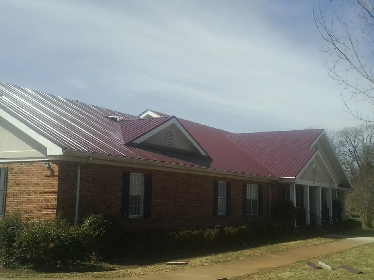 Red metal roof with gabled entries on a long brick building, from a Hail Damage Roof Repair job in Simsbury