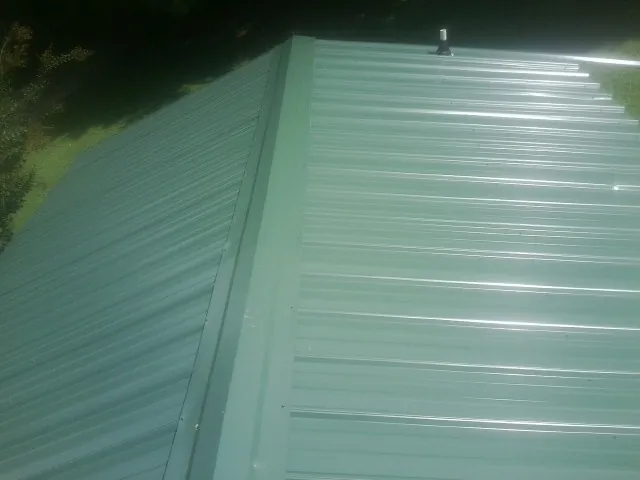 New green metal panels meeting at the ridge of a roof — Flat Roof Repair work by our crew in Simsbury