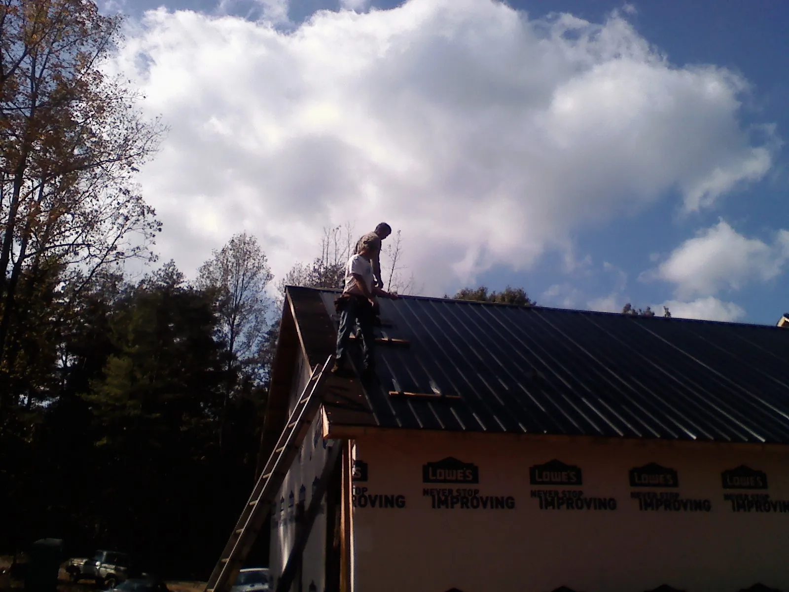 Roofer fastening dark metal panels high against a cloudy sky, from a Roof Inspection job in Simsbury
