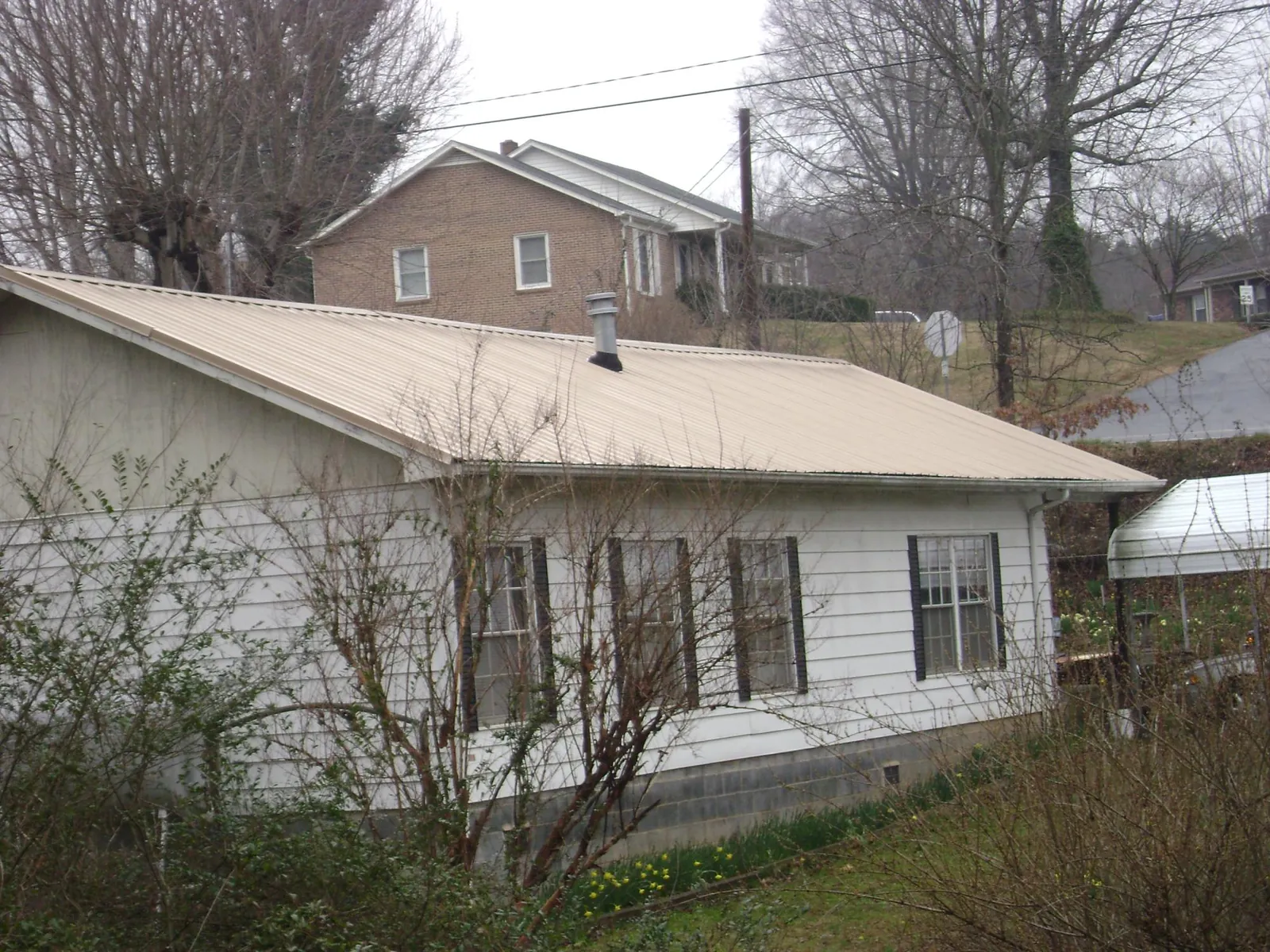 Tan metal roof on a white sided house set into a hillside — Commercial Roofing by Roofing Brothers in Simsbury