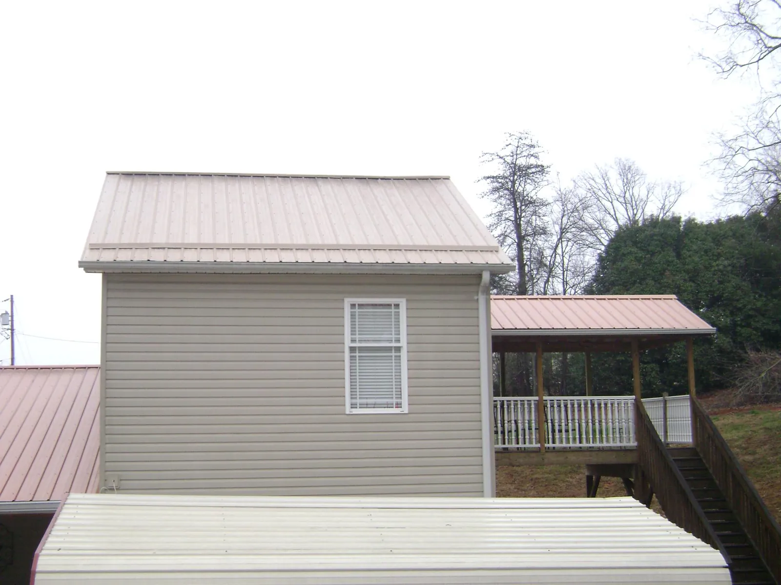 Tan metal roofs on a two story addition and attached porch, from a Roof Replacement job in Simsbury